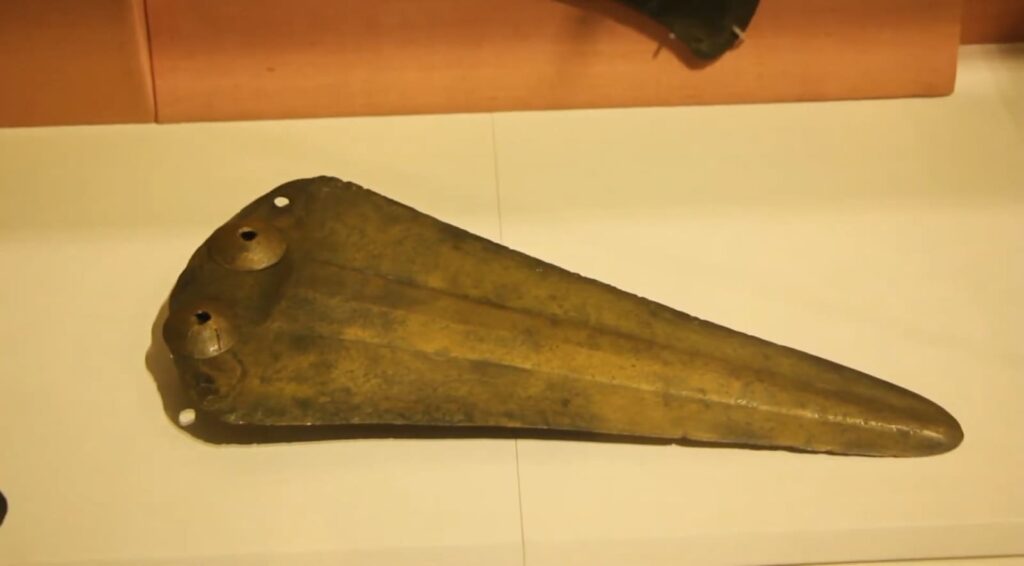 A large, triangular bronze axe head with mounting holes